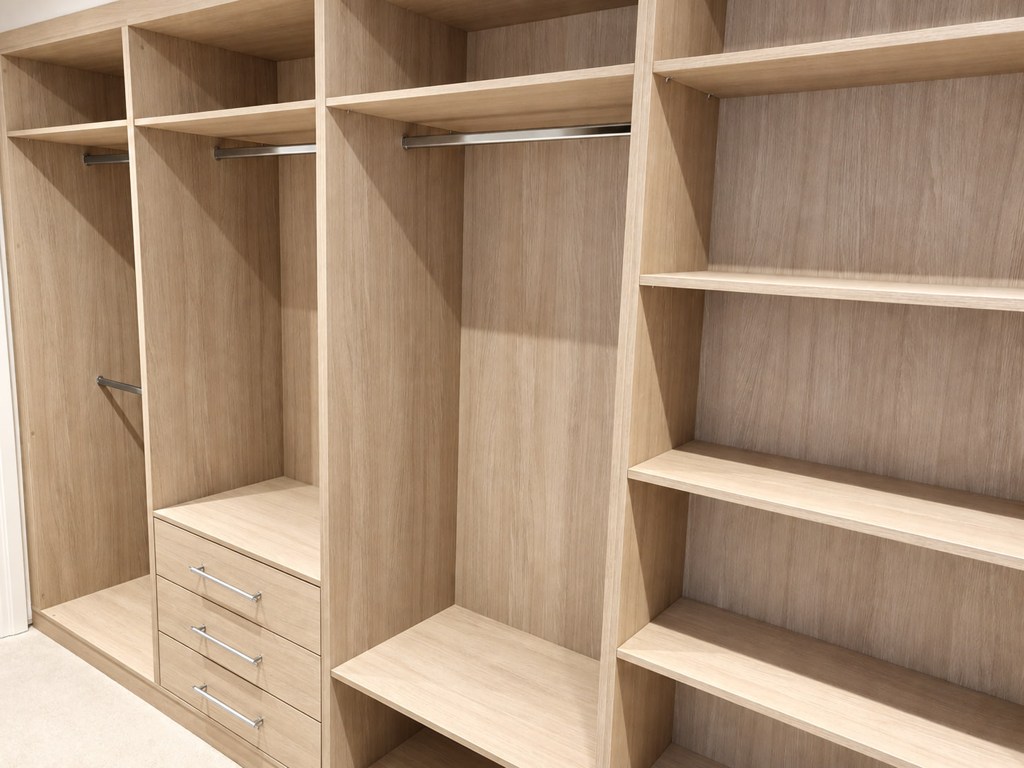 Open light wood fitted wardrobe interior with separate long hanging, short hanging, drawers and adjustable shelves