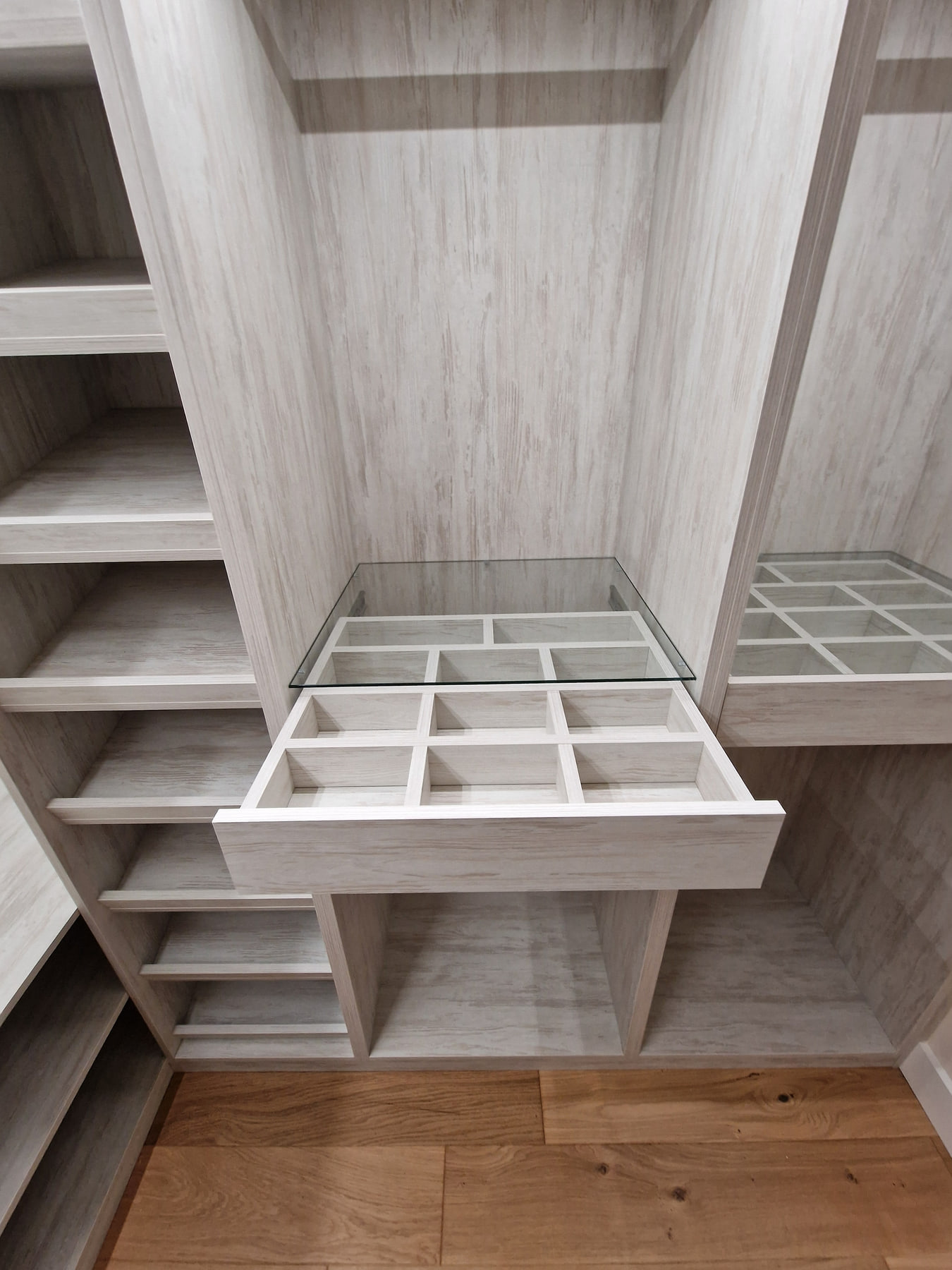 Open glass-top fitted wardrobe accessory drawer with divided compartments beside shoe shelves