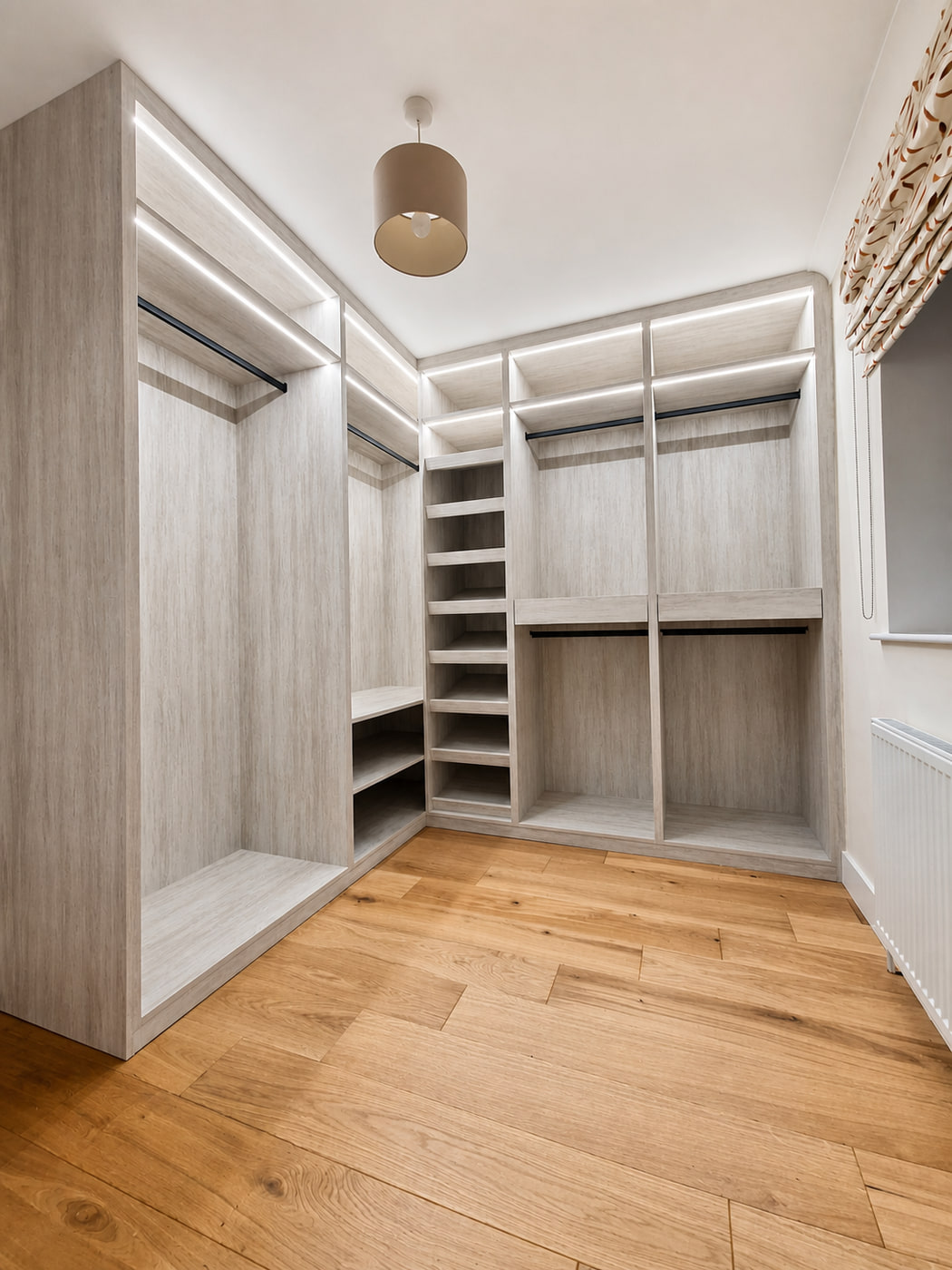 Completed light woodgrain walk-in wardrobe with shelving, drawers, rails and integrated lighting