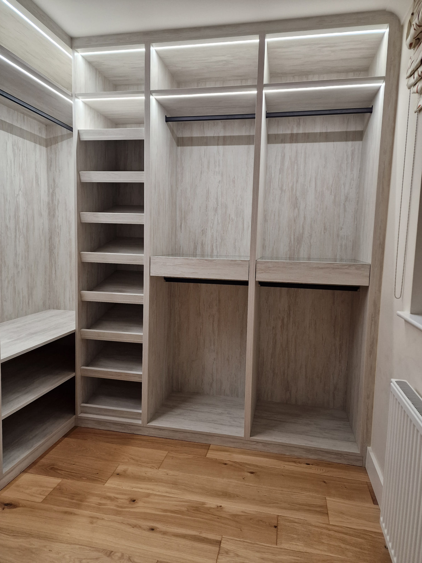 Completed light woodgrain walk-in wardrobe with open hanging, shelves and drawers